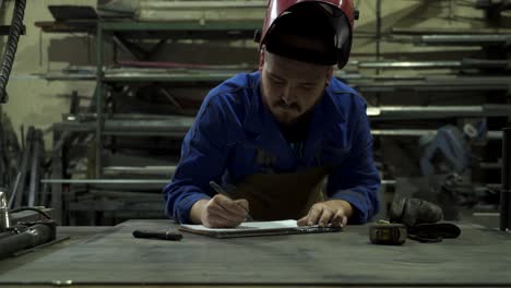 Concentrated-mechanic-in-workshop-writing-notes-in-notepad