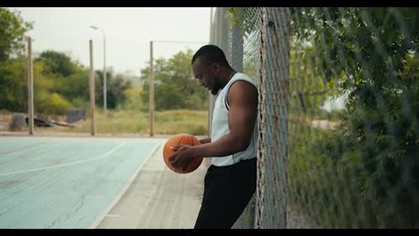 A-young-Black-man-in-a-white-t-shirt-holds-a-basketball-in-his-hands-and-waits-for-his-entry-to-the-basketball-court-to-play.-Substitutes-in-teams-of-sports-games