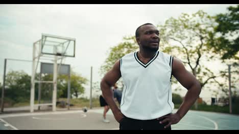 Dynamisches-Porträt-Eines-Schwarzhäutigen-Mannes,-Der-In-Einem-Weißen-T-Shirt-Auf-Einer-Basketballkarte-Vor-Seinen-Freunden-Steht,-Die-Basketball-Spielen