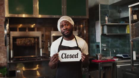 A-Black-person-in-a-doner-market-is-holding-a-Close-sign-and-is-sad-because-the-doner-market-is-closing