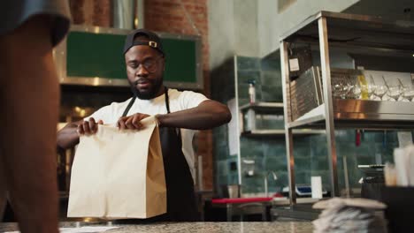 A-Black-person-serves-a-visitor-in-a-doner-market.-A-man-puts-an-order-to-a-customer-in-a-paper-bag.-Attention-to-the-environment