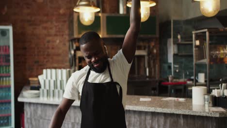 A-waiter-in-a-black-apron-in-a-doner-market-dances-with-wireless-headphones.-Video-filmed-in-high-quality