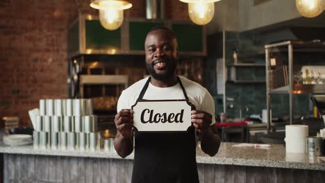 Black-person-guy-in-a-black-apron-holds-a-Close-sign-in-his-hands.-The-establishment-is-closed.-Video-filmed-in-high-quality
