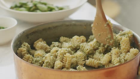 Crop-cook-adding-pesto-sauce-in-pot-with-pasta