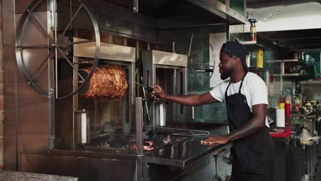 A-man-in-a-black-apron-is-spinning-a-kebab-skewer-at-a-doner-market.-Cooking-meat-according-to-Eastern-standards.-Video-filmed-in-high-quality