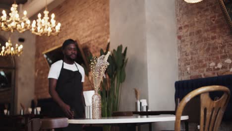 A-Black-person-in-a-black-apron-and-white-T-shirt-places-a-Reserved-sign-on-a-table-in-a-restaurant.-Table-reservation-in-a-restaurant
