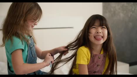 Lovely-little-cute-girl-combing-the-hair-of-her-older-sister-and-while-sitting-on-the-bed,-having-fun