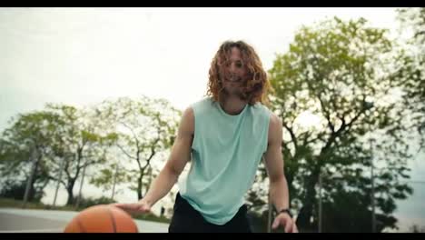 Portrait-of-a-red-haired-curly-haired-man-in-a-light-colored-t-shirt-who-skillfully-dribbles-a-basketball-on-the-basketball-court-outside