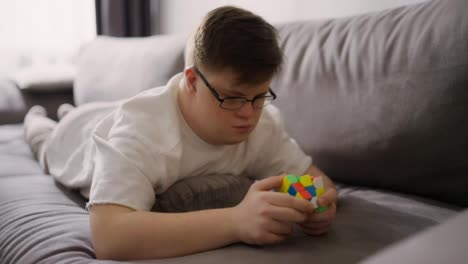 Hombre-Con-Síndrome-De-Down-Descansando-En-El-Sofá-De-Casa-Y-Jugando-Con-Cubo-Rubik