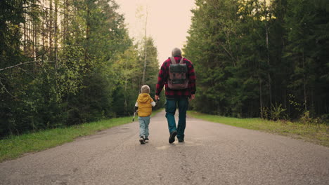 little-boy-and-his-grandfather-are-walking-together-on-road-in-forest-in-spring-or-autumn-day-rear-view