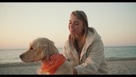 Portrait-of-a-young-blonde-girl-who-strokes-her-dog-in-the-morning-on-the-seashore.-Morning-walk-with-a-pet-on-the-beach-at-sunrise