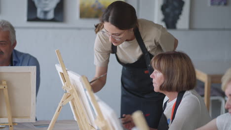High-angle-view-of-cheerful-senior-friends-painting-on-canvas.-Senior-woman-smiling-while-drawing-with-the-group.-Seniors-Attending-Painting-Class-Together.-Senior-men-having-fun-painting-in-art-class