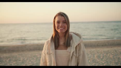 Portrait-of-a-young-beautiful-blonde-girl-who-looks-at-the-camera-and-smiles-against-the-backdrop-of-the-sea-in-the-morning