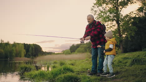 old-fisherman-is-showing-to-his-grandson-how-to-fish-by-rod-grandfather-and-child-are-resting-in-coast-of-lake