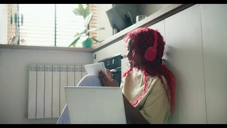 Afroamerikanisches-Mädchen-Mit-Roten-Lockigen-Haaren,-Das-Auf-Dem-Küchenboden-Mit-Laptop-Studiert-Und-Notizen-Macht