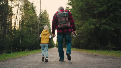 little-boy-and-his-granddad-are-walking-to-fishing-in-morning-strolling-on-picturesque-road-in-coniferous-forest