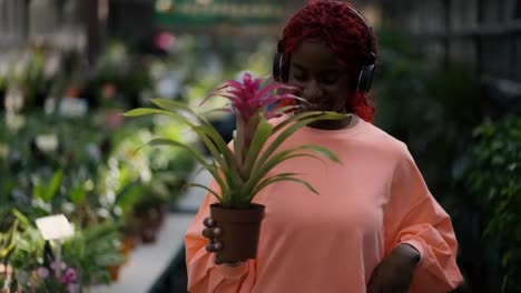 A-african-american-young-girl-in-headphones-is-dancing-with-flower-pot-in-greenhouse