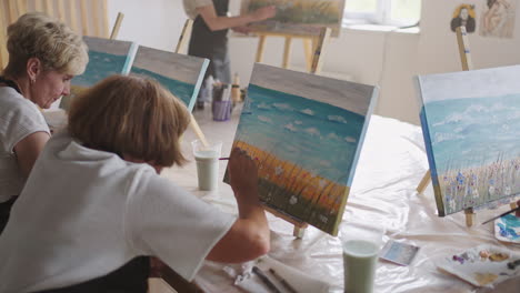 An-old-retired-woman-paints-a-picture-together-with-friends.-An-elderly-group-of-friends-and-a-senior-woman-are-drawing-pictures-together.