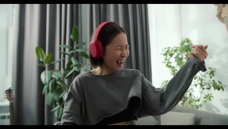 Asian-woman-playing-air-guitar-and-wearing-headphones-to-listen-to-music,-having-fun-at-home
