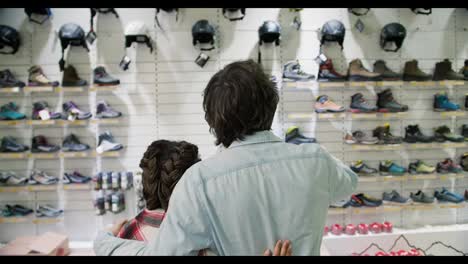 Rear-view-of-a-man-and-woman-choosing-shoes-for-hiking-standing-in-front-beautiful-showcase-on-the-background