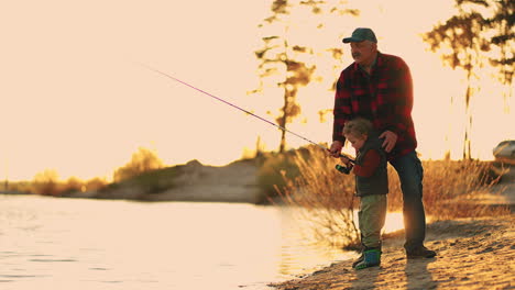 happy-granddad-and-little-grandson-are-catching-fish-by-fishing-rod-in-river-in-sunset