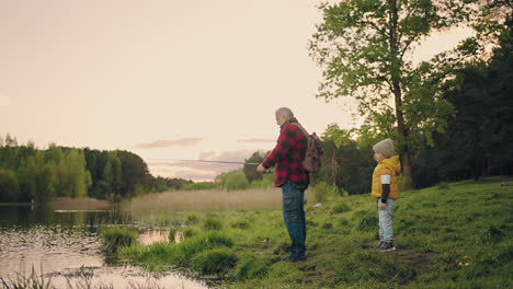 grandpa-and-little-boy-are-fishing-on-coast-of-picturesque-pond-in-woodland-family-weekend