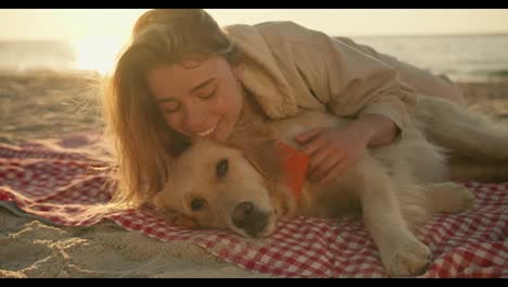 Close-up-shot:-a-blonde-girl-and-her-cute-big-dog-of-light-coloring-lie-side-by-side-on-a-mat-on-a-sunny-beach-in-the-morning.-Happy-time-with-your-pet