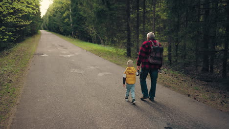 old-man-with-backpack-and-fishing-road-is-walking-and-holding-hand-of-his-little-grandson
