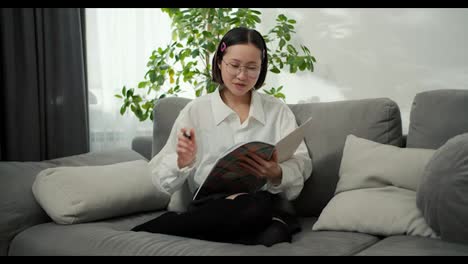 Asiatische-Studentin-Mit-Brille-Liest-Ihr-Notizbuch-Und-Denkt-über-Den-Plan-Zu-Hause-Nach