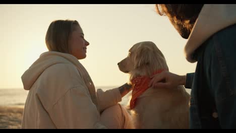 Shooting-up-close:-a-guy-and-a-blonde-girl-are-stroking-a-light-colored-soy-dog-in-the-morning-on-a-sunny-beach.-Beautiful-rays-of-the-sun-in-the-morning