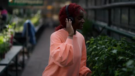 A-african-american-young-girl-in-colorful-blouse-and-headphones-is-dancing-in-flower-greenhouse