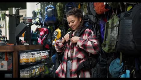 Young-woman-trying-big-tourist-rucksack-in-sports-equipment-store
