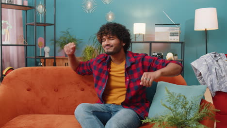Trendy-cheerful-positive-indian-man-dancing-and-moving-to-rhythm-making-dub-dance-gesture-at-home