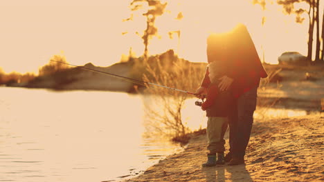 grandfather-is-teaching-his-grandson-to-fish-on-shore-of-lake-in-sunset-happy-family-weekend