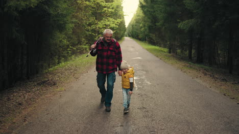 funny-boy-and-his-grandfather-are-walking-to-fishing-strolling-on-road-across-coniferous-forest