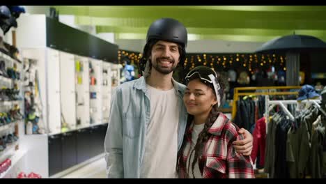 Portrait-of-smiling-couple-posing-in-helmet-and-ski-glasses-during-shopping-in-sport-goods-store