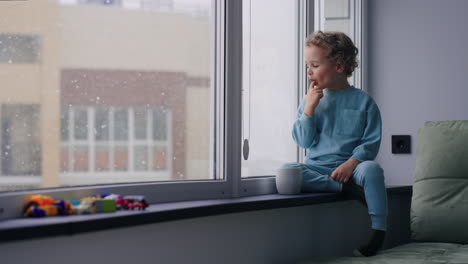 cozy-home-atmosphere-in-winter-weekend-cute-baby-boy-is-sitting-on-windowsill-in-apartment-viewing-snowflakes