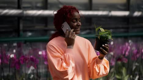 Eine-Glückliche-Afroamerikanische-Frau-Wählt-Topfblumen-Aus,-Die-Sie-Für-Ihren-Garten-Kaufen-Möchte,-Und-Spricht-Per-Handy