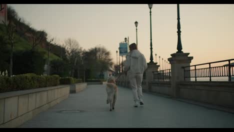 Rear-view-of-a-young-blonde-girl-walking-her-dog-on-the-embankment-at-dawn