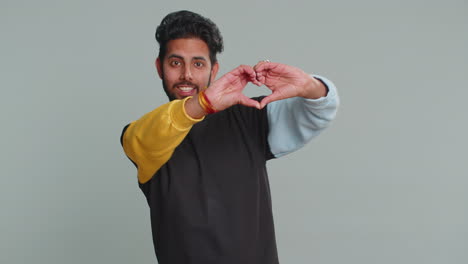 Smiling-hindu-man-makes-heart-gesture-demonstrates-love-sign-expresses-good-feelings-and-sympathy
