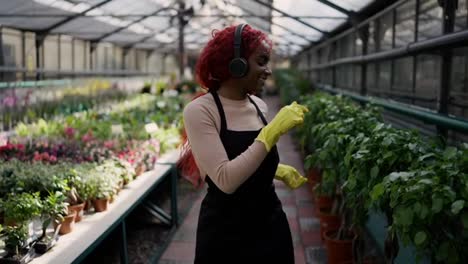 African-american-woman-gardener-florist-walks-through-greenhouse,-dancing-in-good-mood