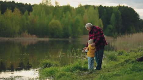 little-boy-is-learning-to-fish-on-lake-shore-loving-grandfather-is-helping
