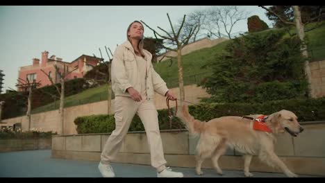 A-young-blonde-girl-in-light-clothes-walks-with-her-light-colored-dog-on-the-embankment-in-nature.-Morning-walk-with-pet