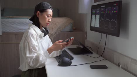 Asian-broker-analyzing-graphics-on-monitor-and-smartphone