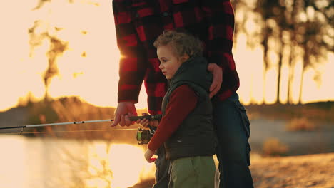 happy-little-boy-with-curly-hair-is-fishing-by-rod-granddad-or-father-is-helping-child