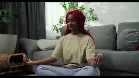 Young-stylish-african-american-woman-sitting-in-lotus-position-with-closed-eyes-healthy-calm-girl-relaxing-in-meditation
