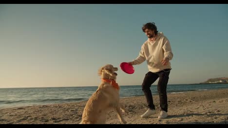 Nahaufnahme-Eines-Jungen-Mannes,-Der-Morgens-Am-Sonnigen-Strand-Mit-Seinem-Hund-In-Heller-Farbe-Und-Einem-Roten-Spielzeug-Spielt