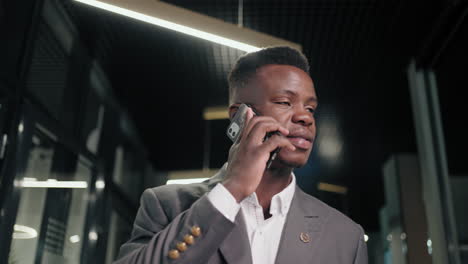 African-Business-man-talking-smartphone-in-office-interior.-Smiling-black-businessman-calling-mobile-phone-in-corridor.-Portrait-of-friendly-african-american-man-walking-in-business-center-hallway.