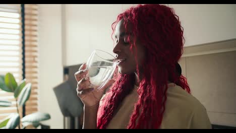 Lockige,-Fröhliche-Afroamerikanische-Frau,-Die-Morgens-Ein-Glas-Frisches-Wasser-Trinkt