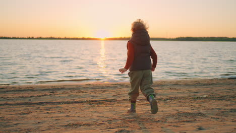playful-curly-child-is-running-on-river-shore-in-spring-sunset-time-happiness-and-childhood-moments